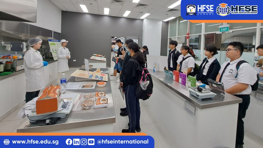 A group of secondary students in a food laboratory, listening to their teacher.