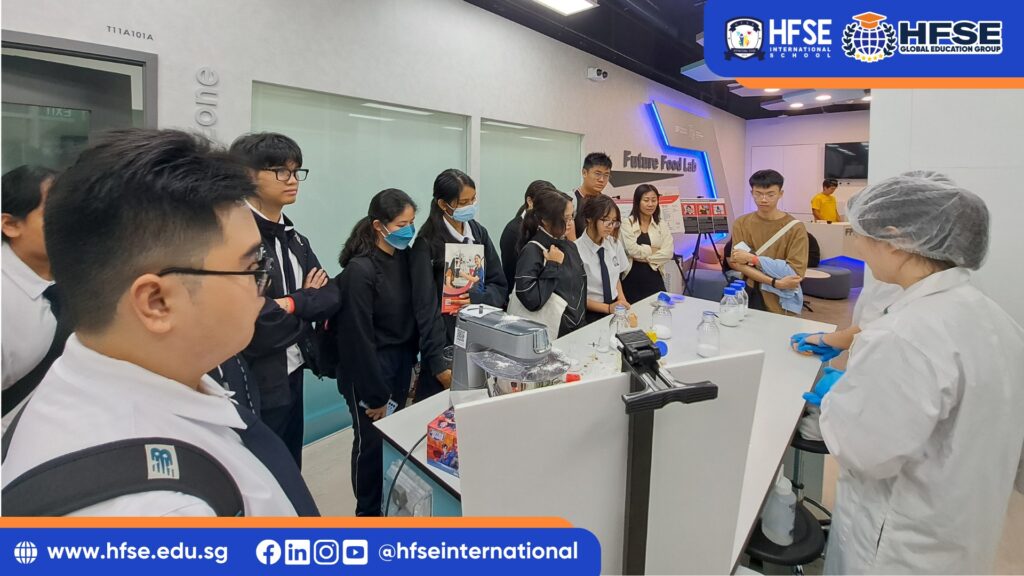 A group of secondary students in a food laboratory, observing a teacher.