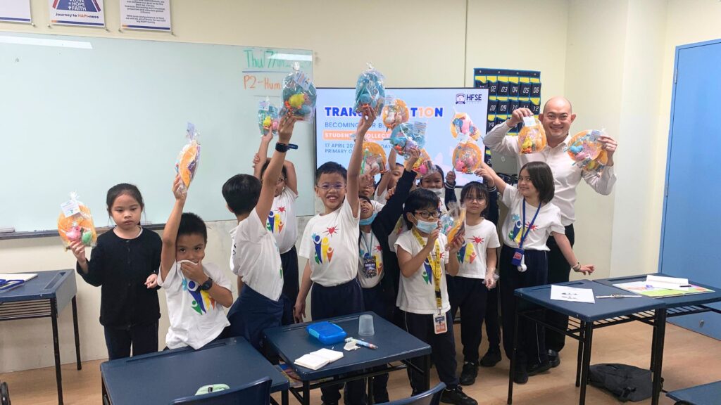 A group of primary school students in Singapore raising their hands and posing for a photo together.