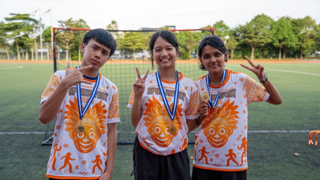 A group of secondary school students in Singapore wearing orange team sportsfest T-shirts and flashing peace signs while posing for a group photo.