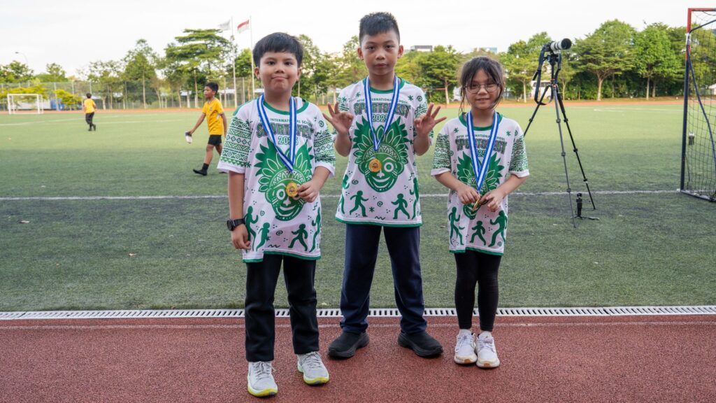 A group of primary school students in Singapore wearing green team sportsfest T-shirts and posing for a photo.